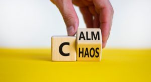 Stop chaos, time to calm. Male hand turns a wooden cube and changes the word 'chaos' to 'calm'. Beautiful yellow table, white background, copy space. Business and chaos or calm concept.