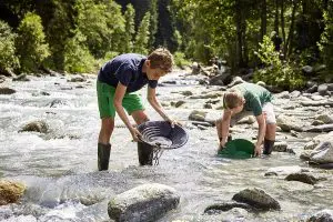 2 Jungs im Fluss, die sich wohl eher spielerisch mit Hilfe von Sieben auf die Suche nach Gold machen